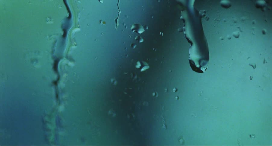 Water is running down a glass window and there is a light blue light on inside