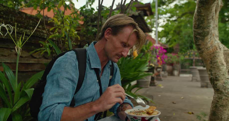 A man eating a bowl of food while sitting on a sidewalk curb