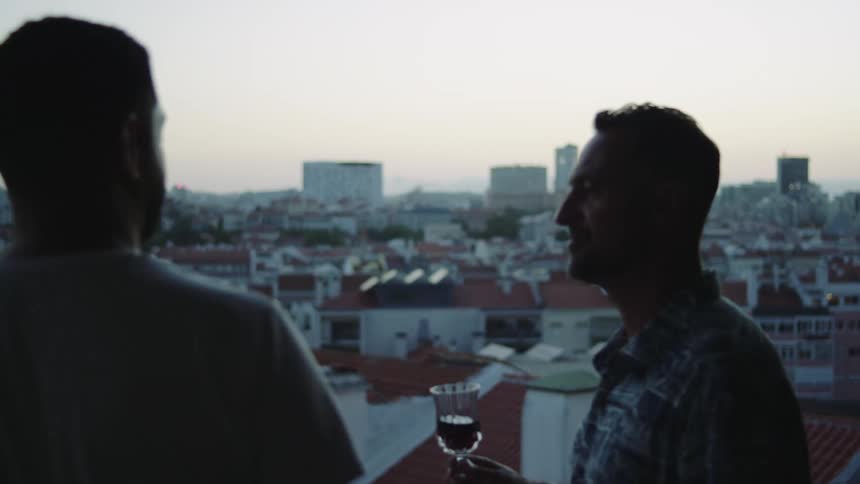 Two men laugh while drinking wine on their balcony