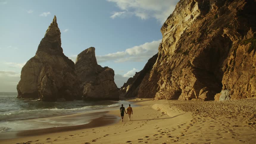 A couple hold hands while walking on the beach