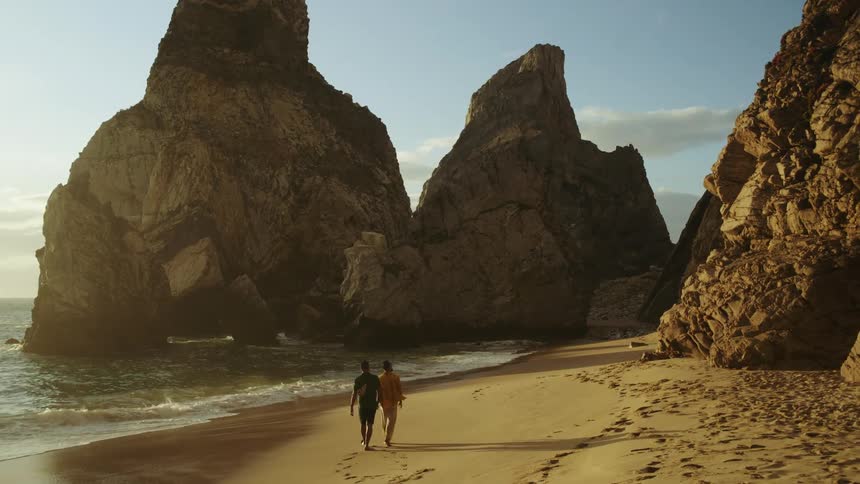 Two men holding hands while strolling on asandy beach