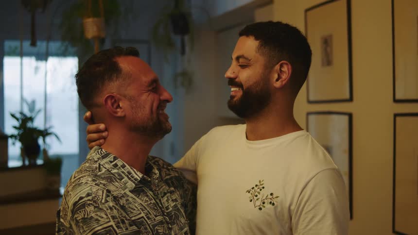 Two men kiss and hug in their living room