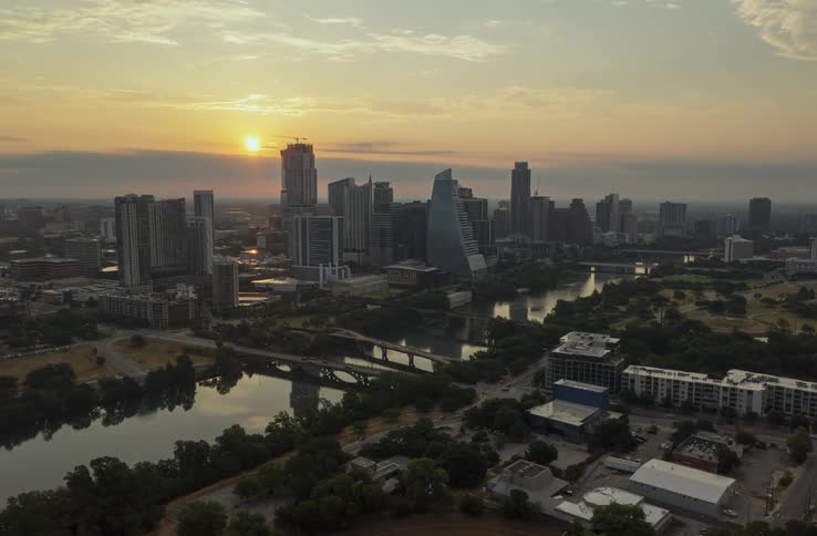 Towers and skyscrapers stand tall over the city and reflect on the water of the lake going through town as the sun sets in the distance