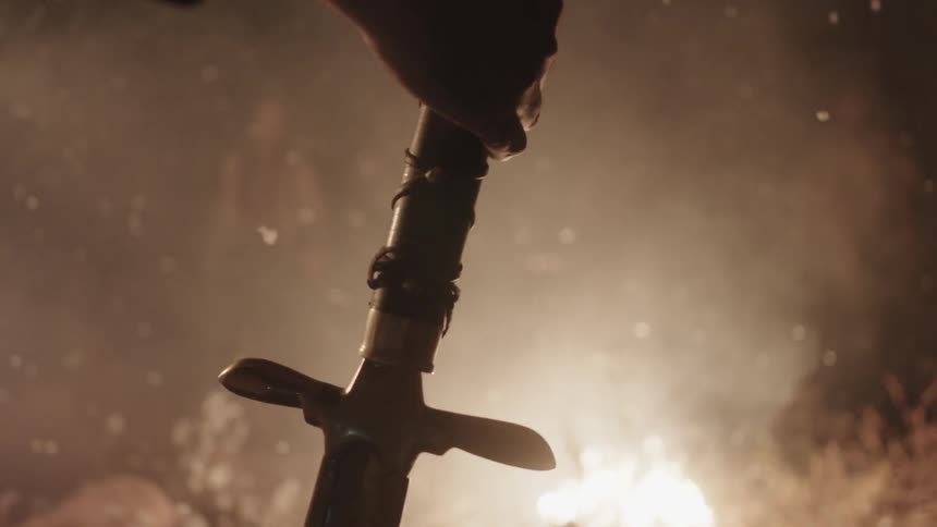 People stand by a fire one has a sword