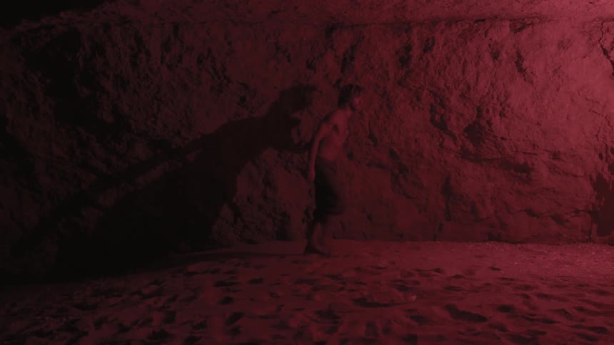 A man walks through a dark cave with flickering light