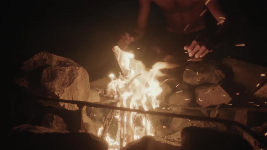 A man adds wood to a campfire and warms his hands