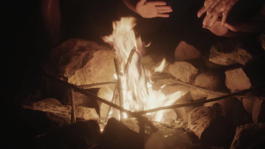 People warm themselves by a fire at night