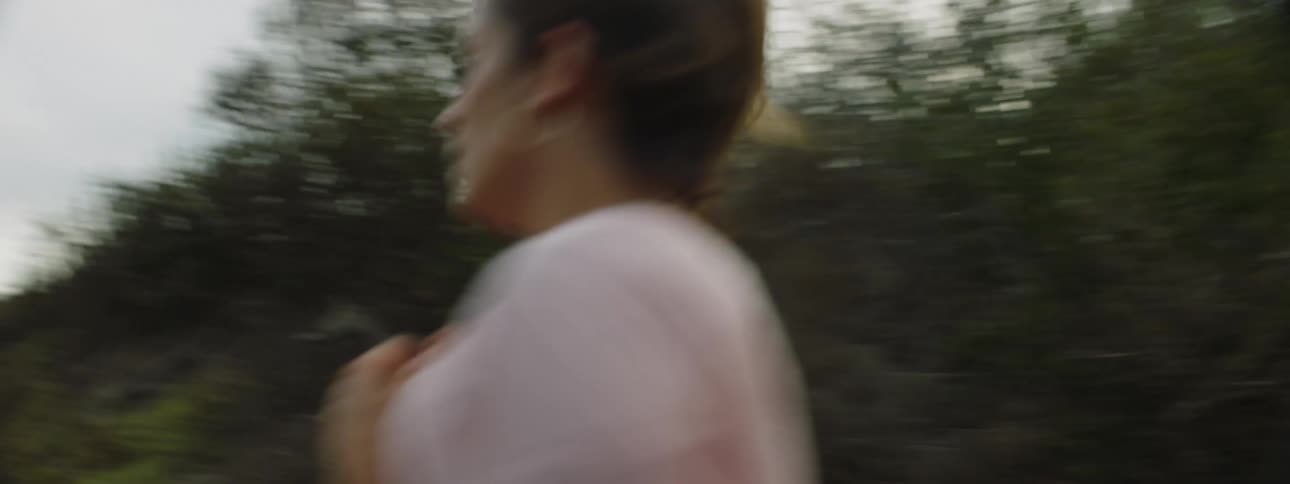 Woman jogs toward the ocean passing between hills onto the beach