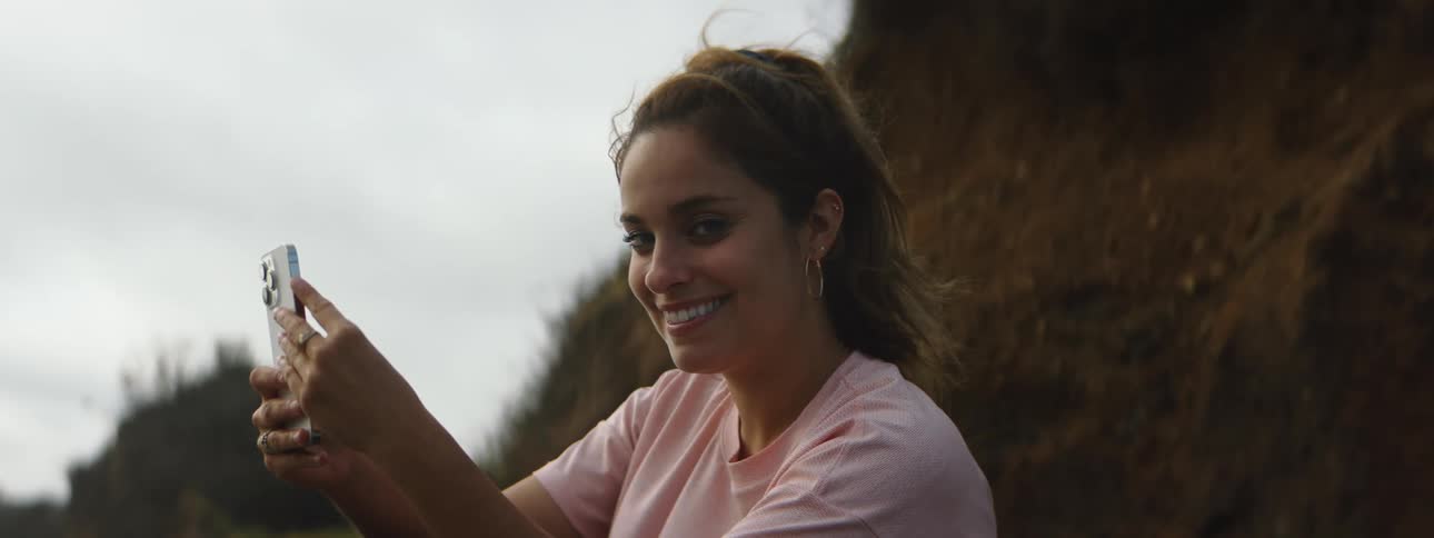 Woman with brown ponytail pink t shirt takes photo with smartphone looking and winking at camera