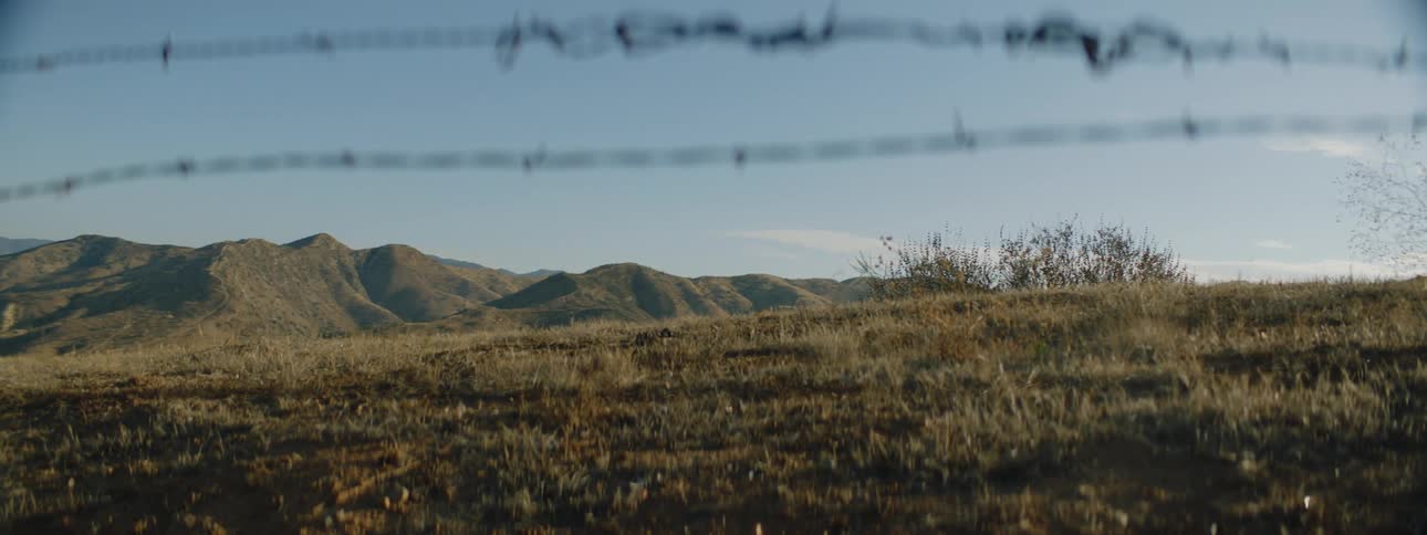 Hill and distant mountains seen from behind barbed wire