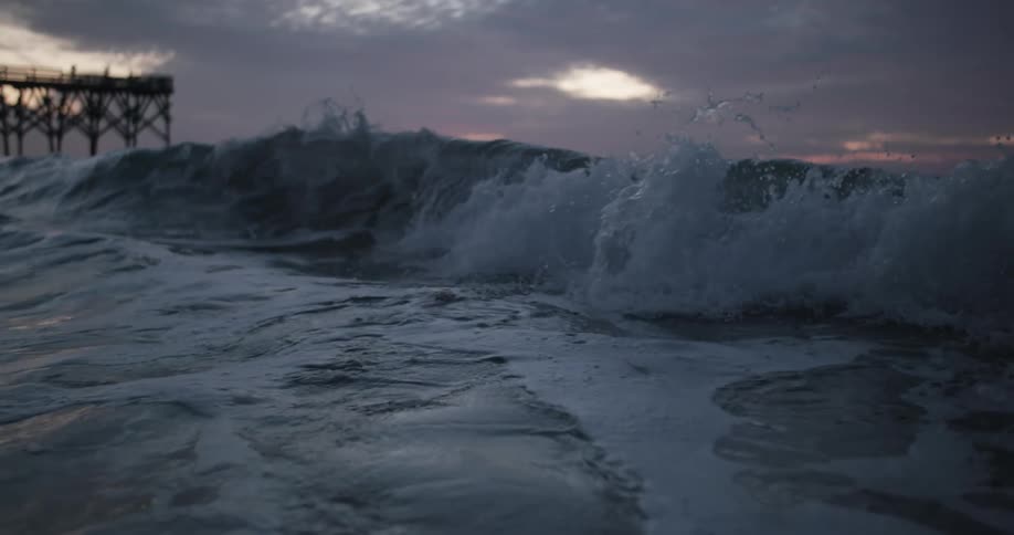 The silhouette of a pier behind a curling splashing wave