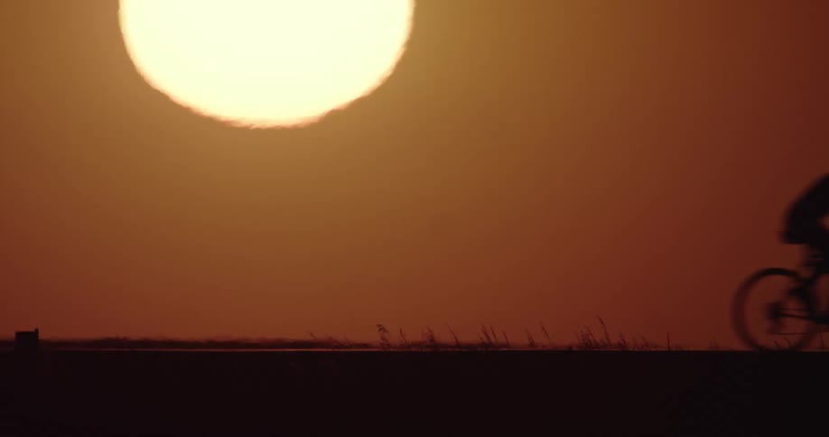 Silhouette of a man riding a bicycle in the countryside in front of the setting sun