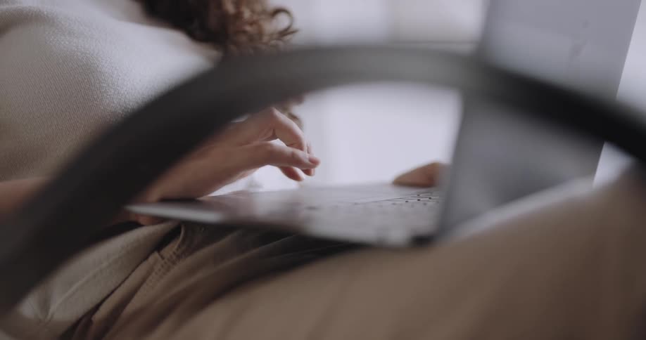 A woman types on a laptop that is in her lap