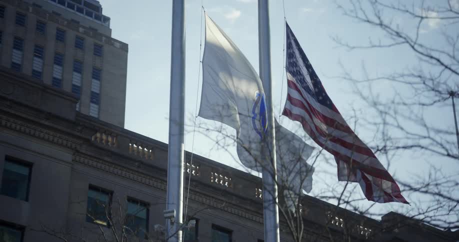 The american flag and massachusetts state flag flying at half mast in front of a building