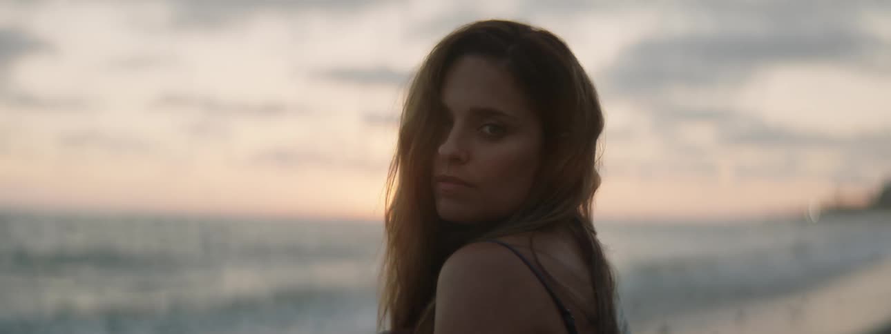 A woman on the beach turns her head and looks around