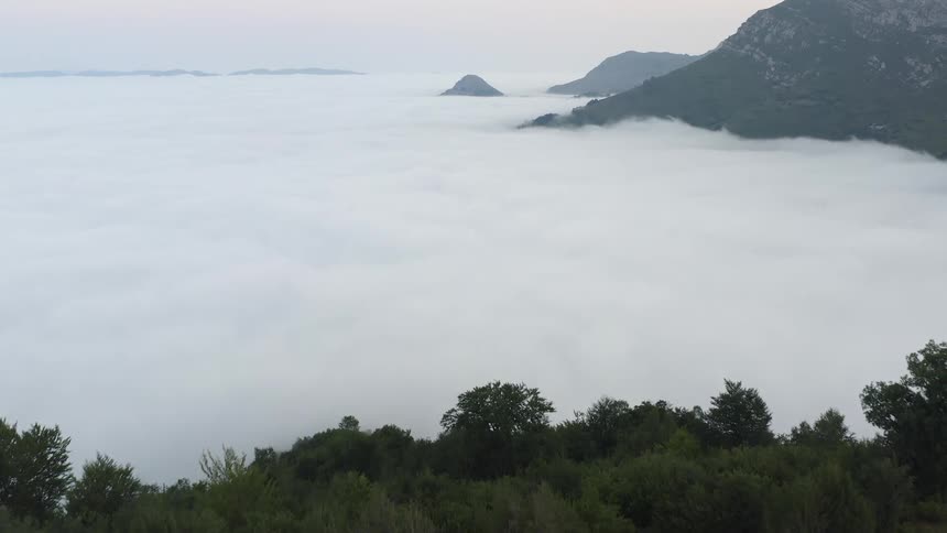Mountain huts are scattered in the countryside next to mountains covered in clouds in Northern Spain