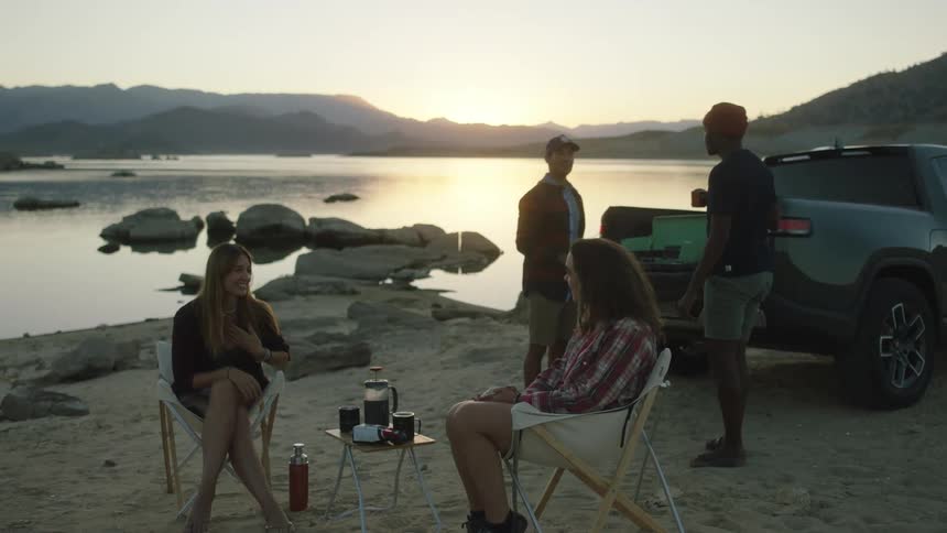 Four friends talk and have fun on the sand near a lake