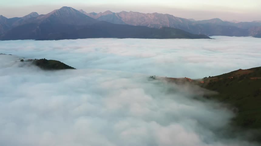 Thick fog fills the valley as sunlight shines on mountains under a hazy sky of Northern Spain