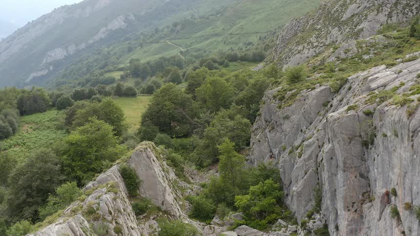 Trees and rocks in a deep ravine between rock formations with Asturian mountains in the distance