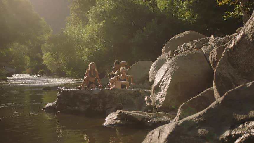 A small group of people are sitting on rocks and boulders in a river surrounded by trees