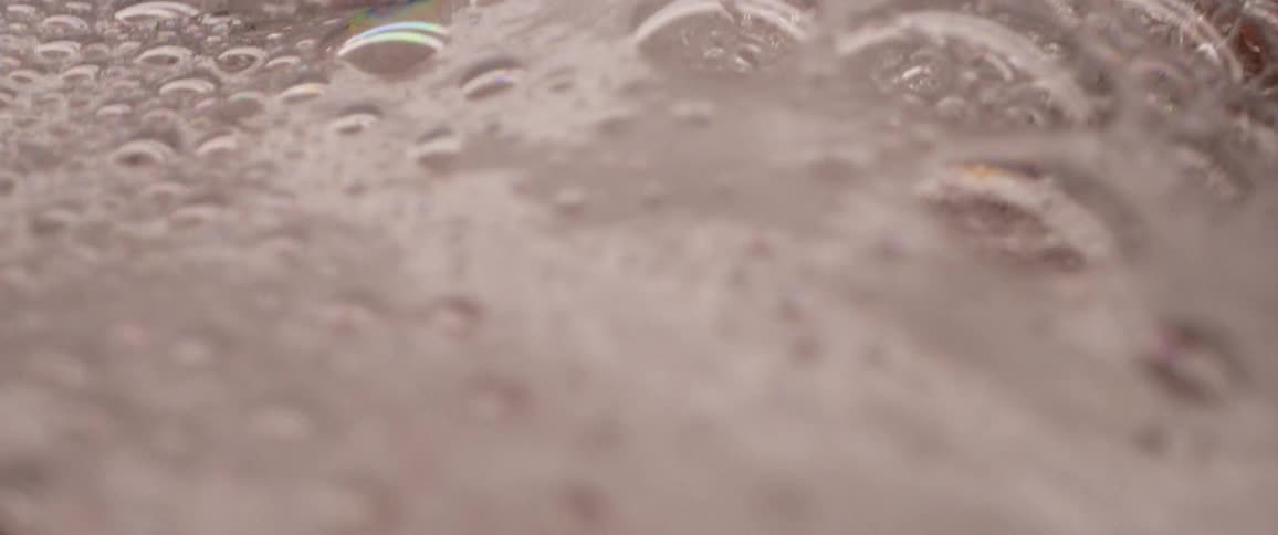 A faucet is pouring water into a basin full of water that is extremely soapy with lots of bubbles
