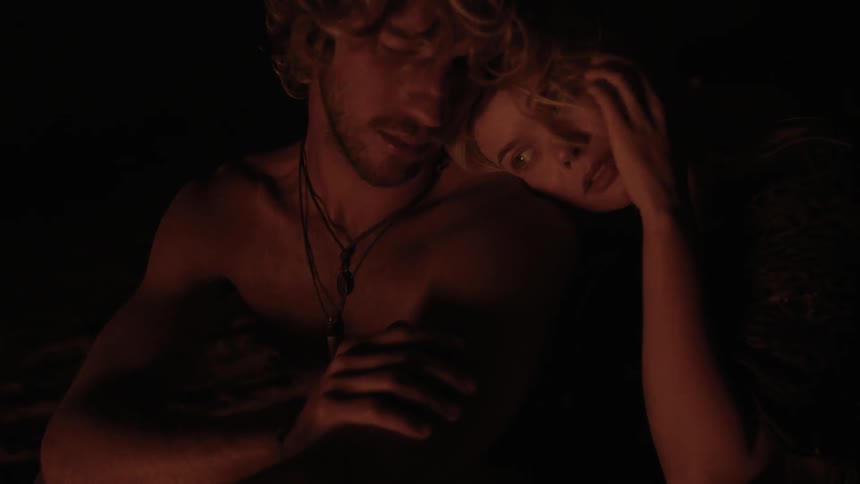 A man and women lean on each other by a fire at night