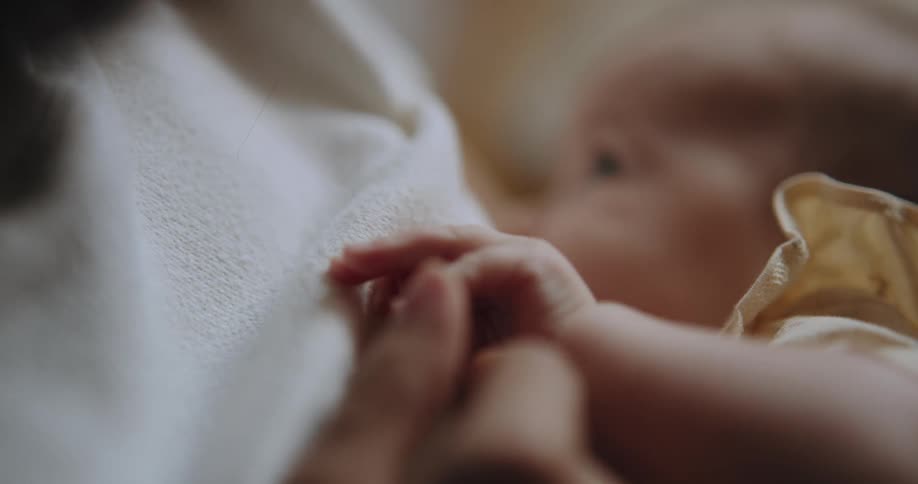 A baby her mothers hand while breastfeeding