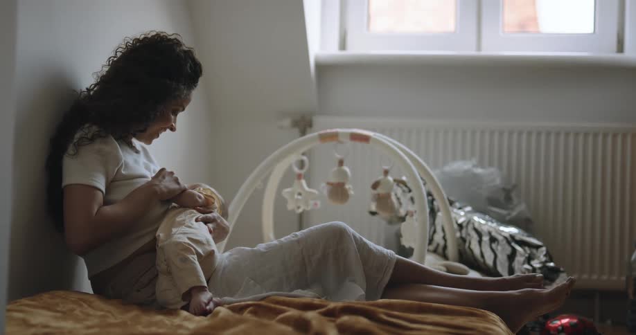 Mother sits against wall smiling as she holds child