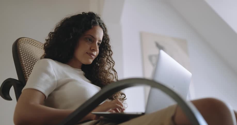 A woman works on her laptop while sitting in a rocking chair