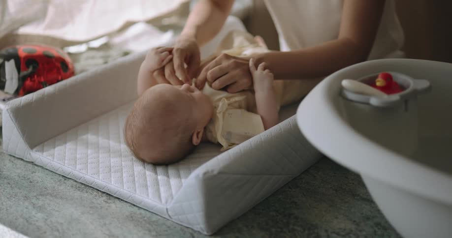 Mother with curly hair white shirt and earrings takes off babys clothes lying on changing mat