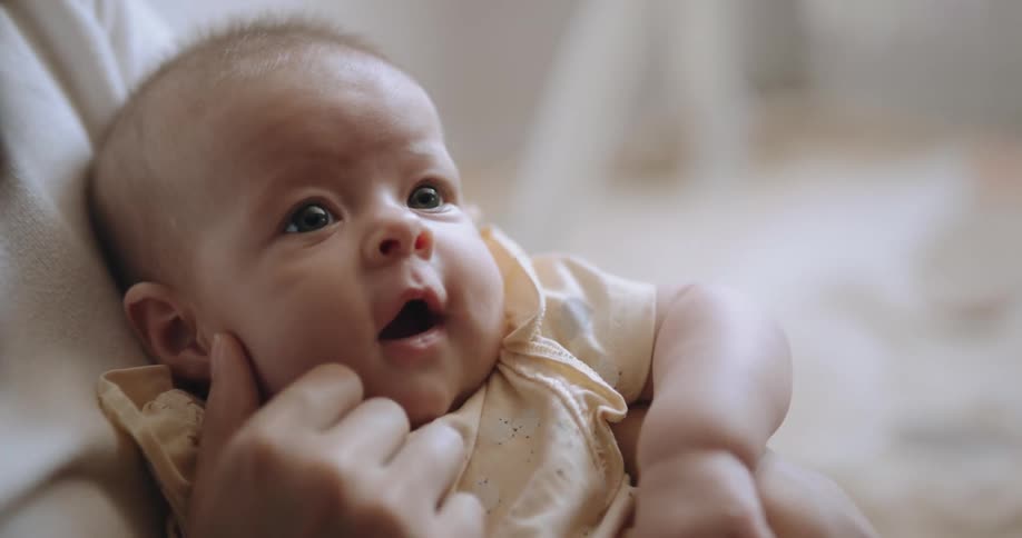 A woman is holding her baby in her arms and strokes their face with her hand