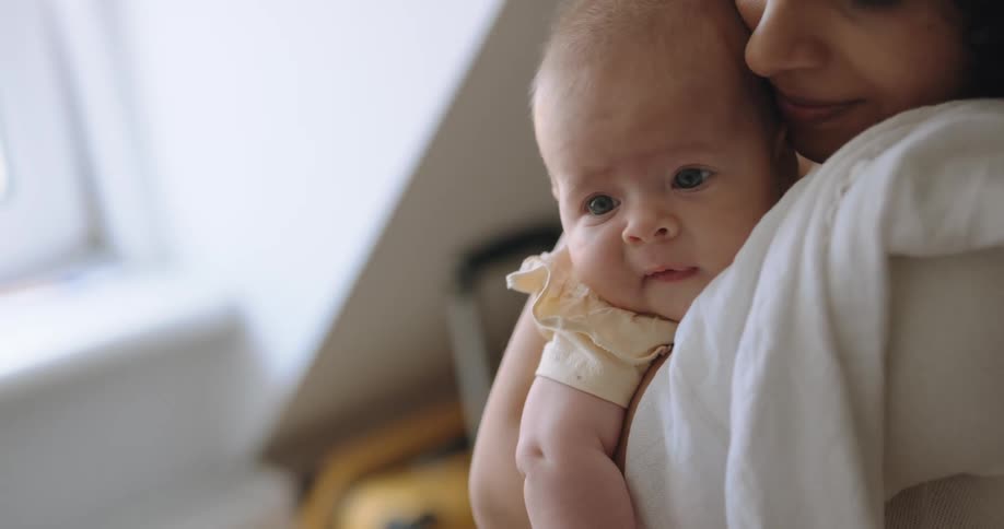 Happy mother with curly hair and white shirt holds newborn baby