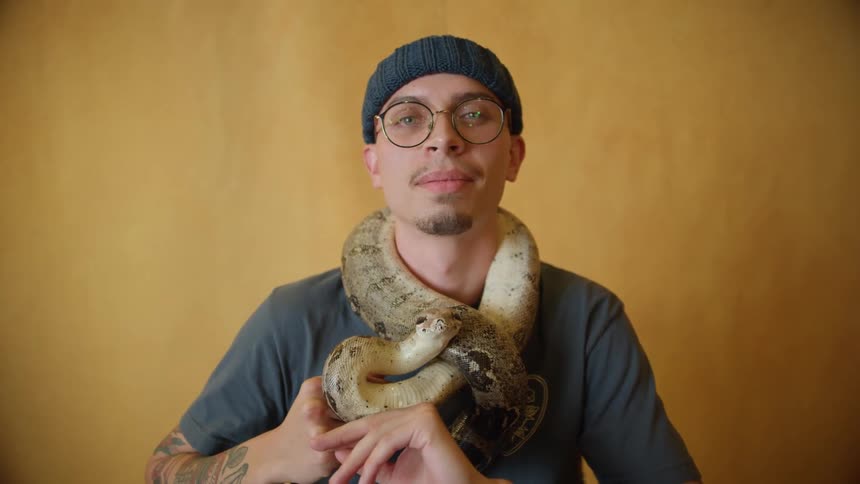 A man holds a snake and poses straightforward to the camera
