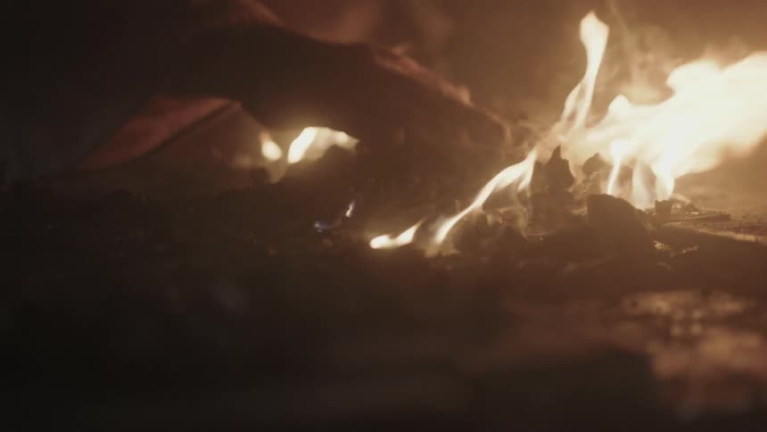 A man arranges the ashes in a fire using his bare hand