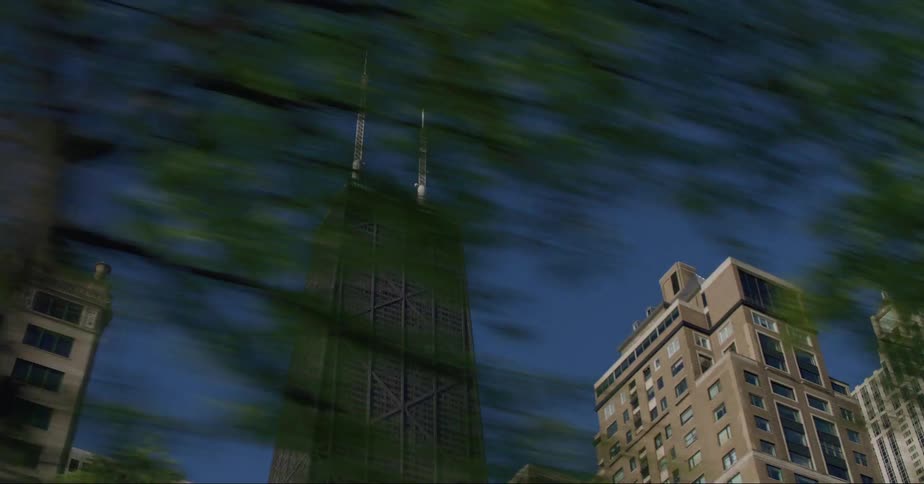 The john hancock building in chicago against a bright blue sky through the trees from street level
