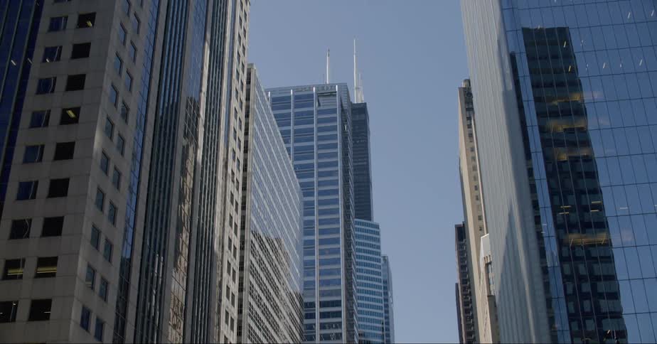 Road passes through downtown between skyscrapers that reflect each other and the sky