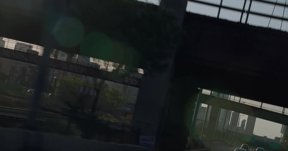 Distant skyscrapers and high rise buildings seen from vehicle driving on highway passing under overpass