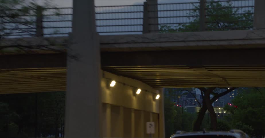 Distant skyscrapers and high rise buildings seen from vehicle driving on highway passing under overpass at dusk