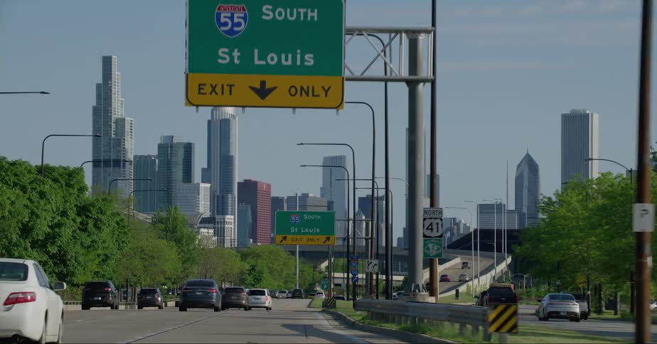 Vehicle drives on highway with guide signs and high rise buildings in the background in the city