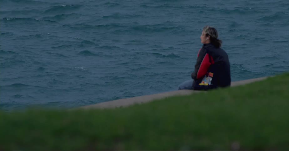 A woman deep in thought while sitting on a waterfront curb