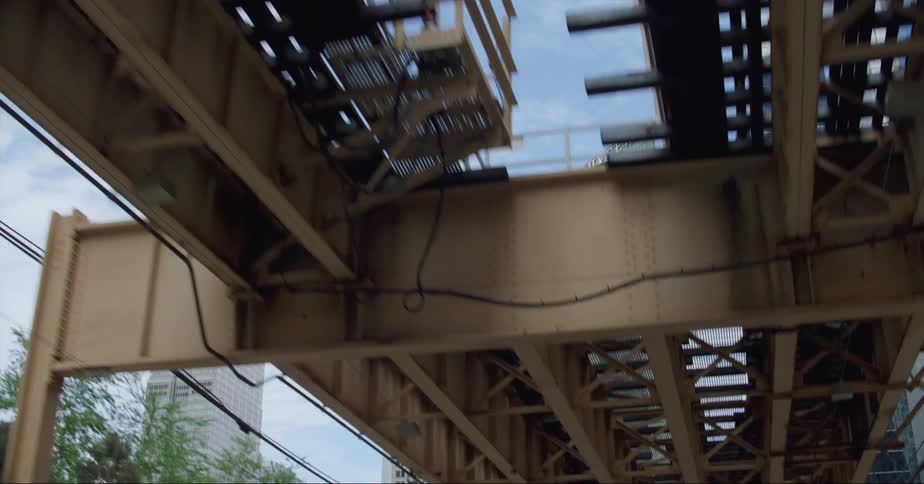Pedestrians walk along sidewalk paralleling elevated train track near downtown skyscrapers