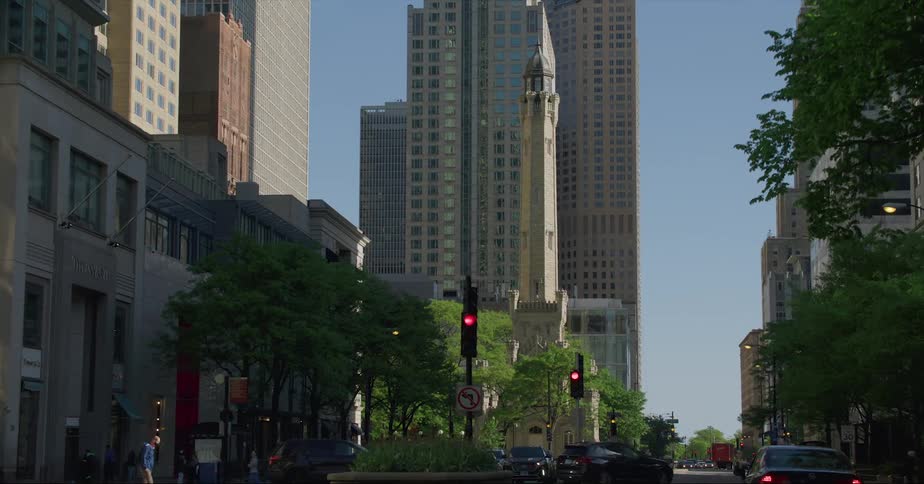 People walk across streets in a busy city with cars driving and office buildings in the distance