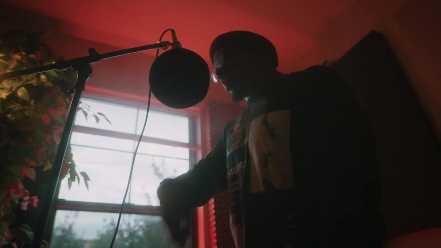 A man stands and raps in front of a large microphone in a studio