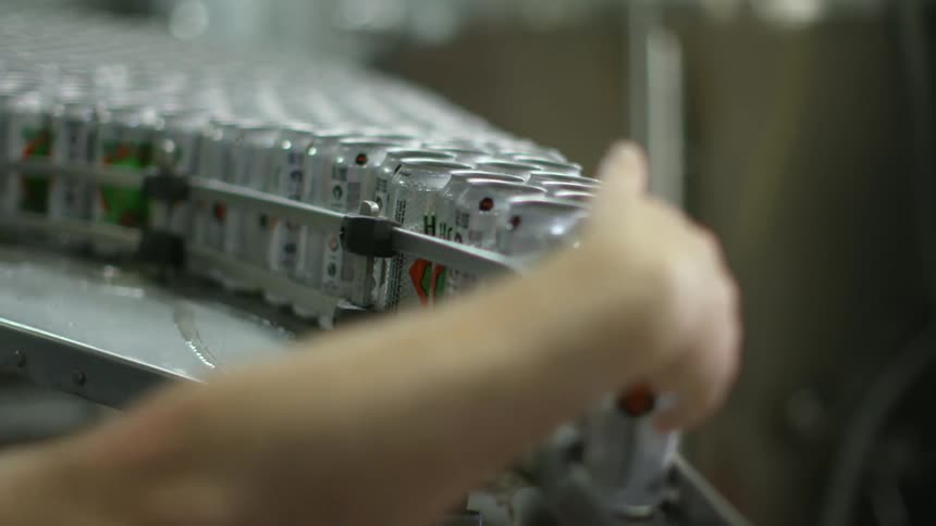 A woman in a factory guides cans down a conveyor belt