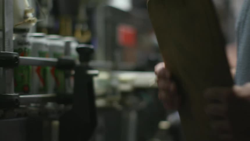 A man in a factory writes on a clipboard and then places a lid on a can