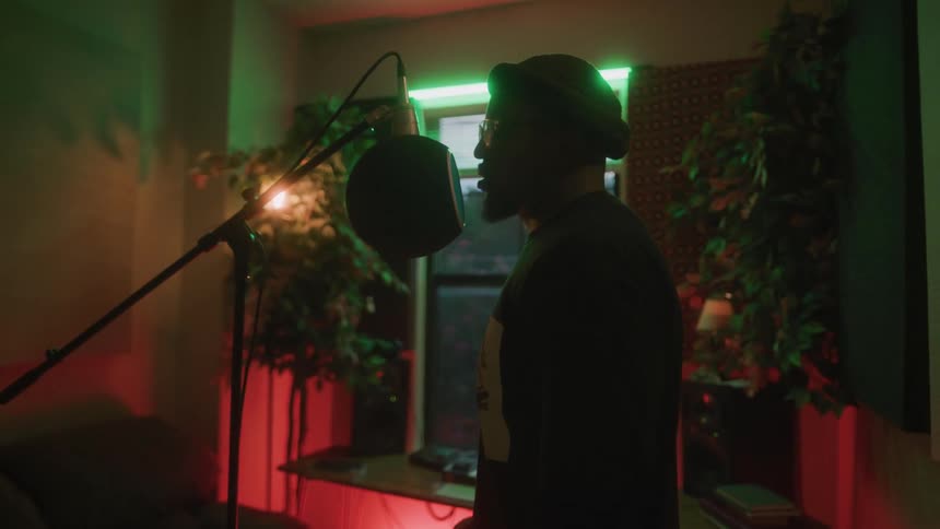A man standing in his home studio singing and recording into a professional microphone