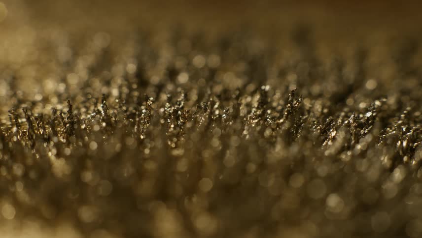 Iron filings covered in gold dust rise and move in spikes under a magnetic field