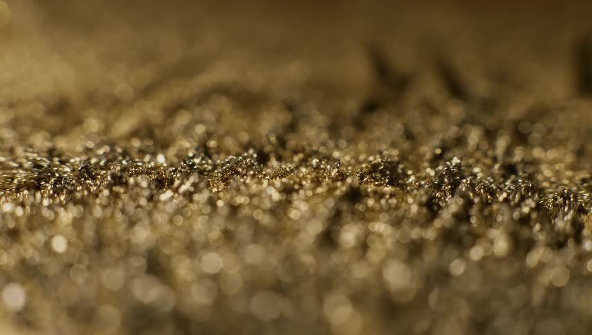 Extreme close up of iron fillings mixed with gold dust moving and spiking under the influence of a magnetic field