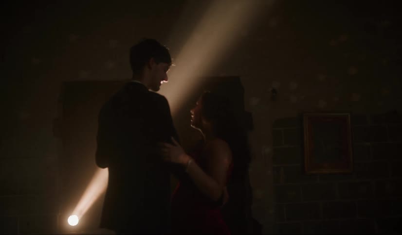 Light shines on a disco ball on the ceiling as two teenagers are dancing in a dark empty room