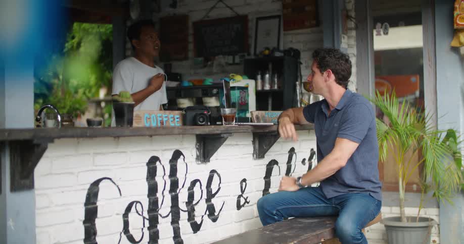 A man sits at a coffee bar signing back and forth with a man working the bar